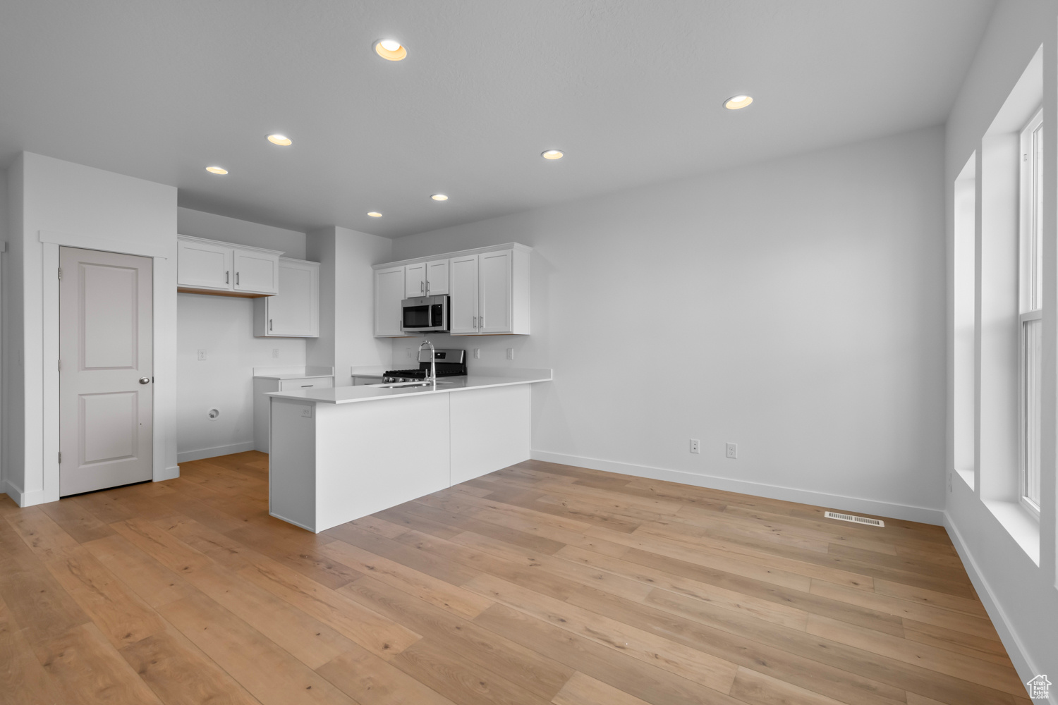 Kitchen featuring kitchen peninsula, stainless steel appliances, a healthy amount of sunlight, white cabinets, and light wood-type flooring