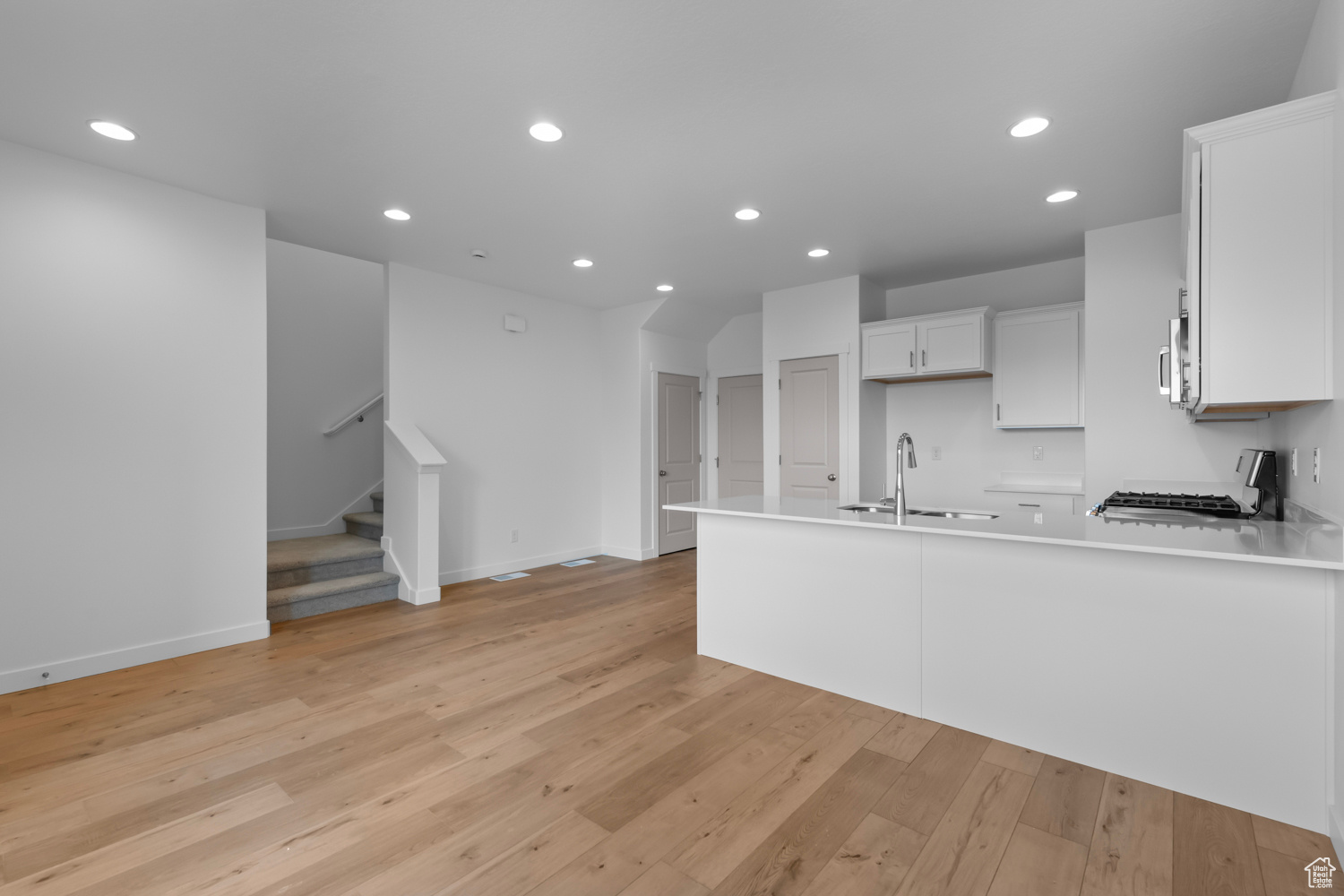 Kitchen featuring kitchen peninsula, light hardwood / wood-style floors, range, white cabinetry, and sink