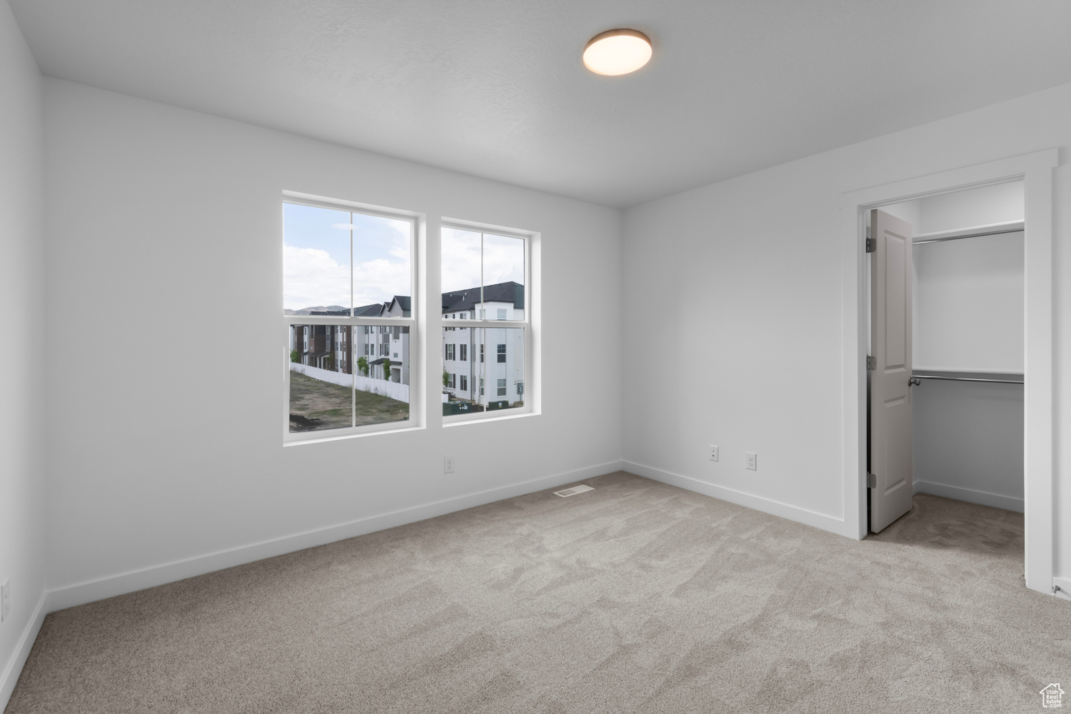 Unfurnished bedroom featuring light colored carpet, a walk in closet, and a closet