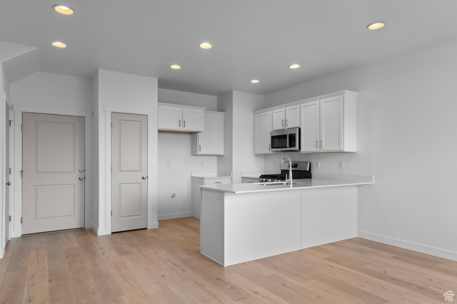 Kitchen with white cabinets, stainless steel appliances, kitchen peninsula, and light wood-type flooring