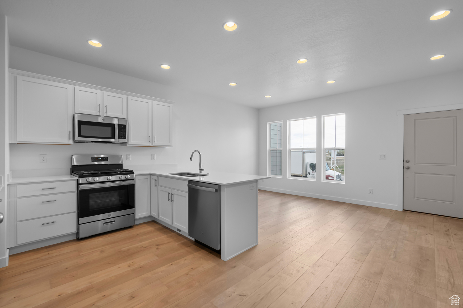 Kitchen with sink, light hardwood / wood-style floors, white cabinetry, stainless steel appliances, and kitchen peninsula