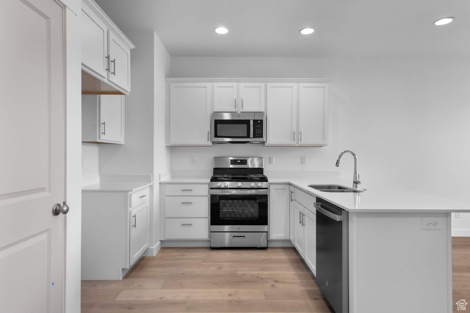 Kitchen with white cabinets, light hardwood / wood-style flooring, kitchen peninsula, appliances with stainless steel finishes, and sink