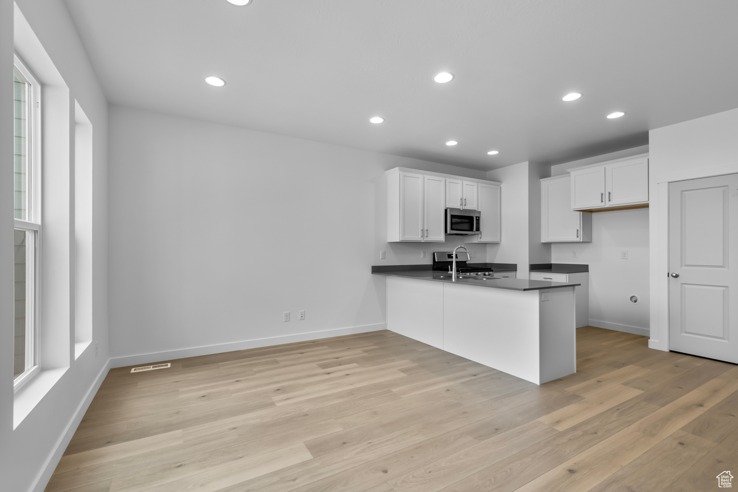 Kitchen featuring light hardwood / wood-style flooring, kitchen peninsula, white cabinetry, and stainless steel appliances