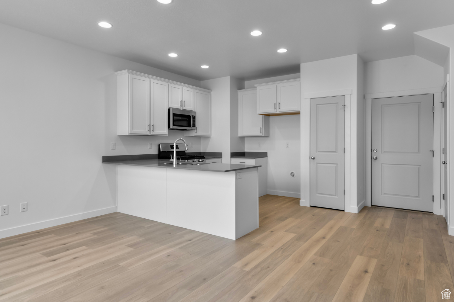 Kitchen with light hardwood / wood-style flooring, range, kitchen peninsula, and white cabinetry