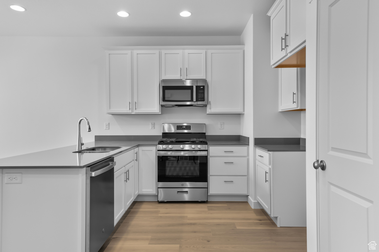 Kitchen with kitchen peninsula, appliances with stainless steel finishes, white cabinetry, sink, and light wood-type flooring