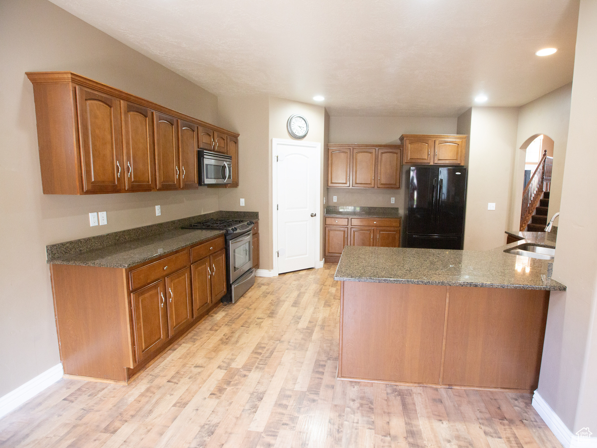 Kitchen with dark stone countertops, stainless steel appliances, sink, and light wood-type flooring