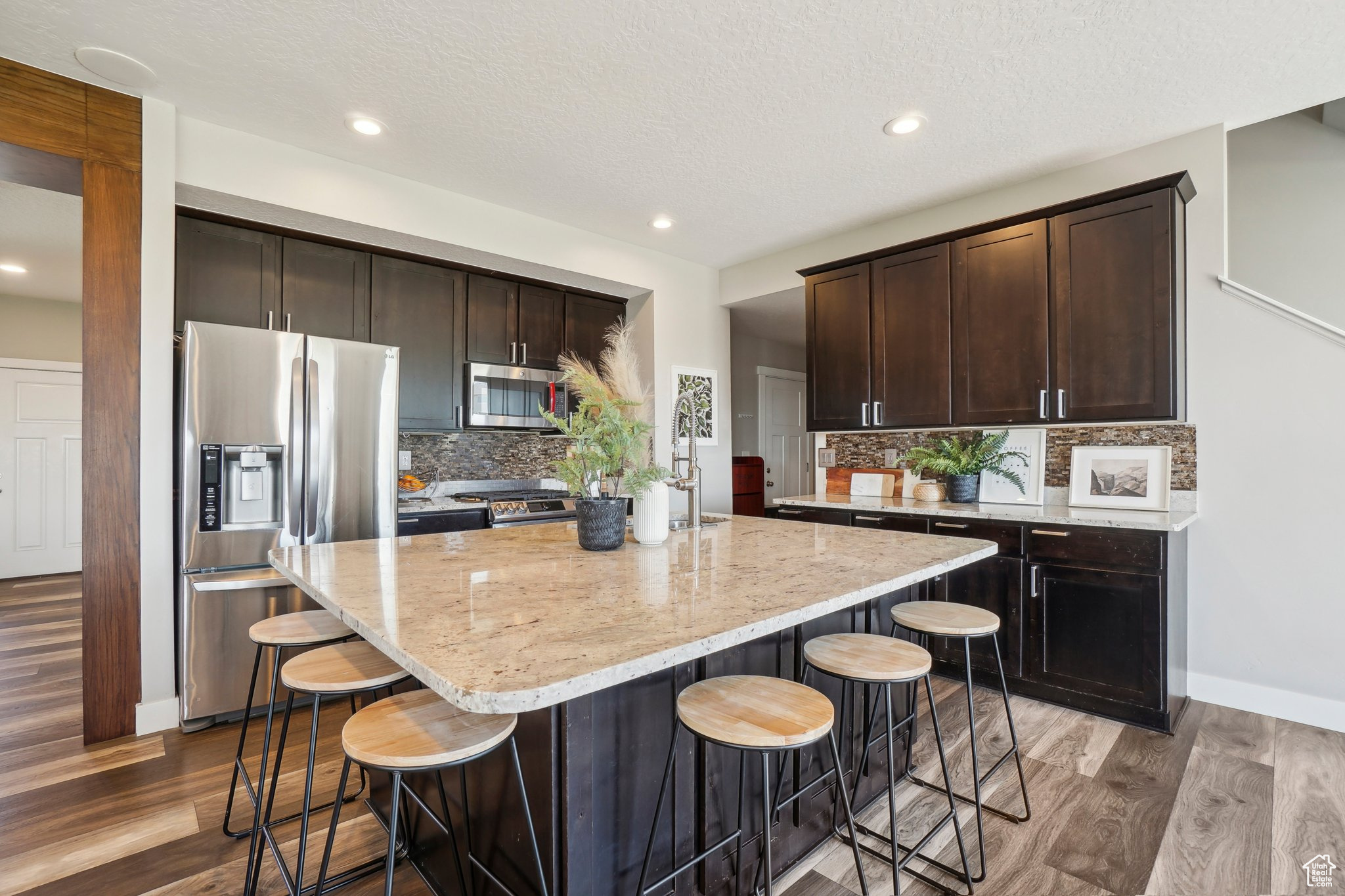 Kitchen featuring a kitchen breakfast bar, tasteful backsplash, wood-type flooring, a center island, and appliances with stainless steel finishes