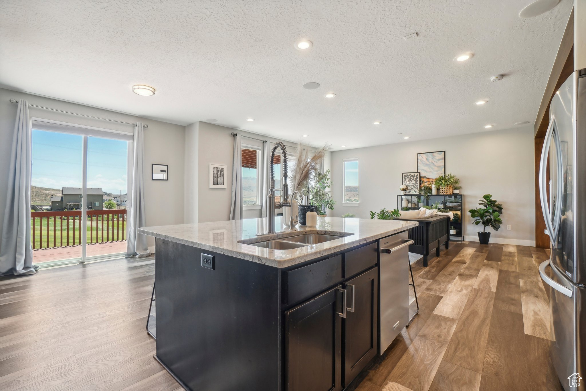 Kitchen featuring light hardwood / wood-style floors, a textured ceiling, a kitchen island with sink, and appliances with stainless steel finishes