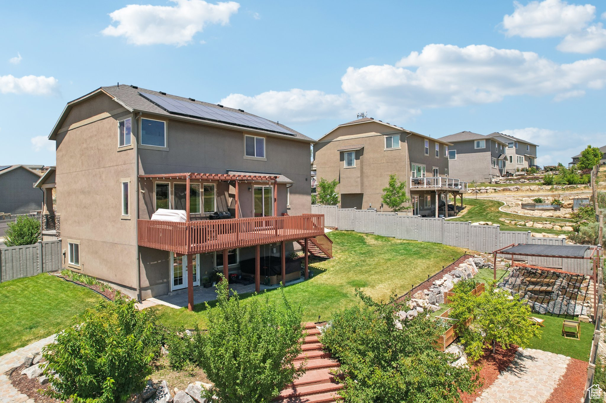 Rear view of house with a deck, a pergola, a lawn, and solar panels