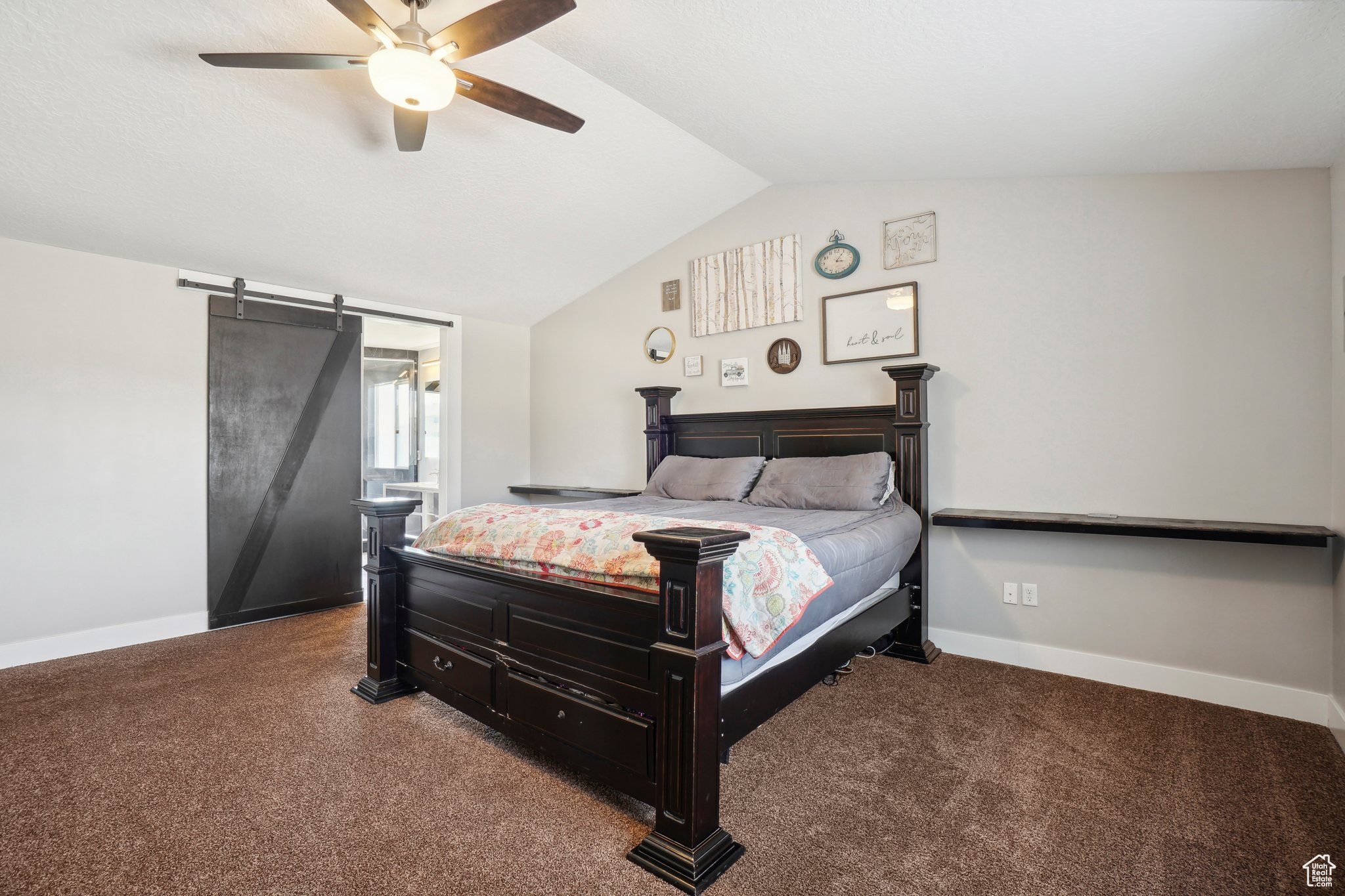 Carpeted bedroom featuring a barn door, ceiling fan, and lofted ceiling