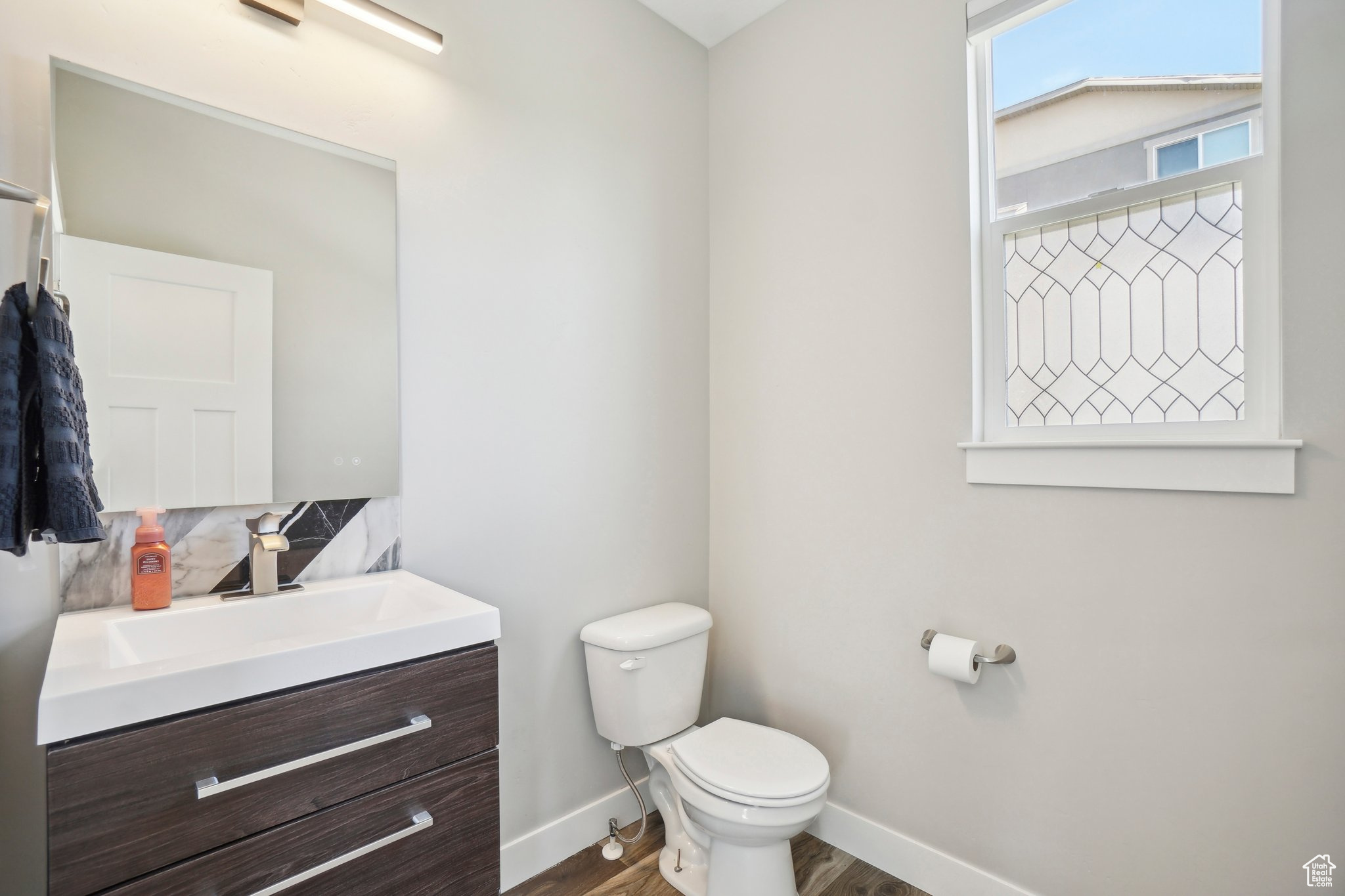 Bathroom with wood-type flooring, vanity, toilet, and tasteful backsplash