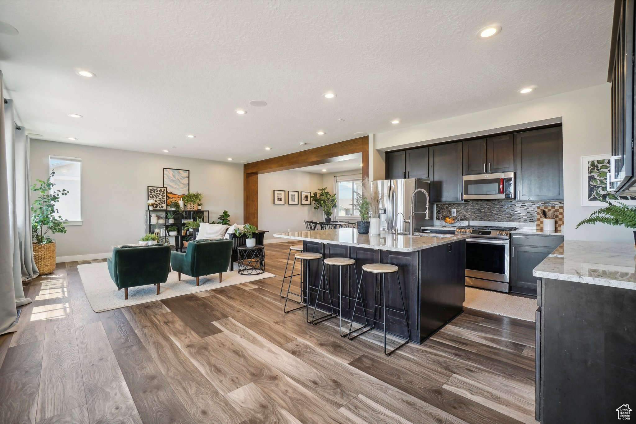 Kitchen featuring tasteful backsplash, an island with sink, stainless steel appliances, wood-type flooring, and light stone counters