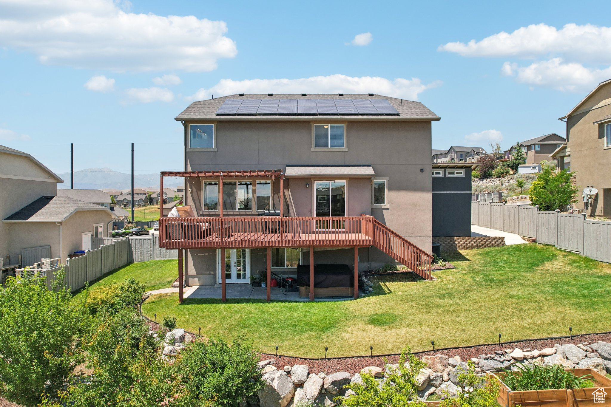 Rear view of house featuring a deck, a lawn, a patio, and solar panels