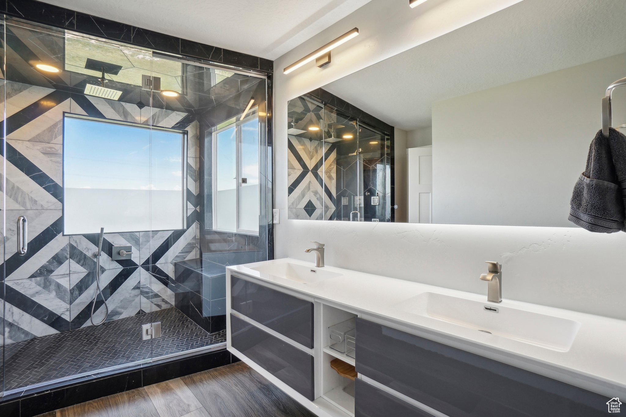 Bathroom featuring a shower with shower door, dual vanity, and hardwood / wood-style flooring