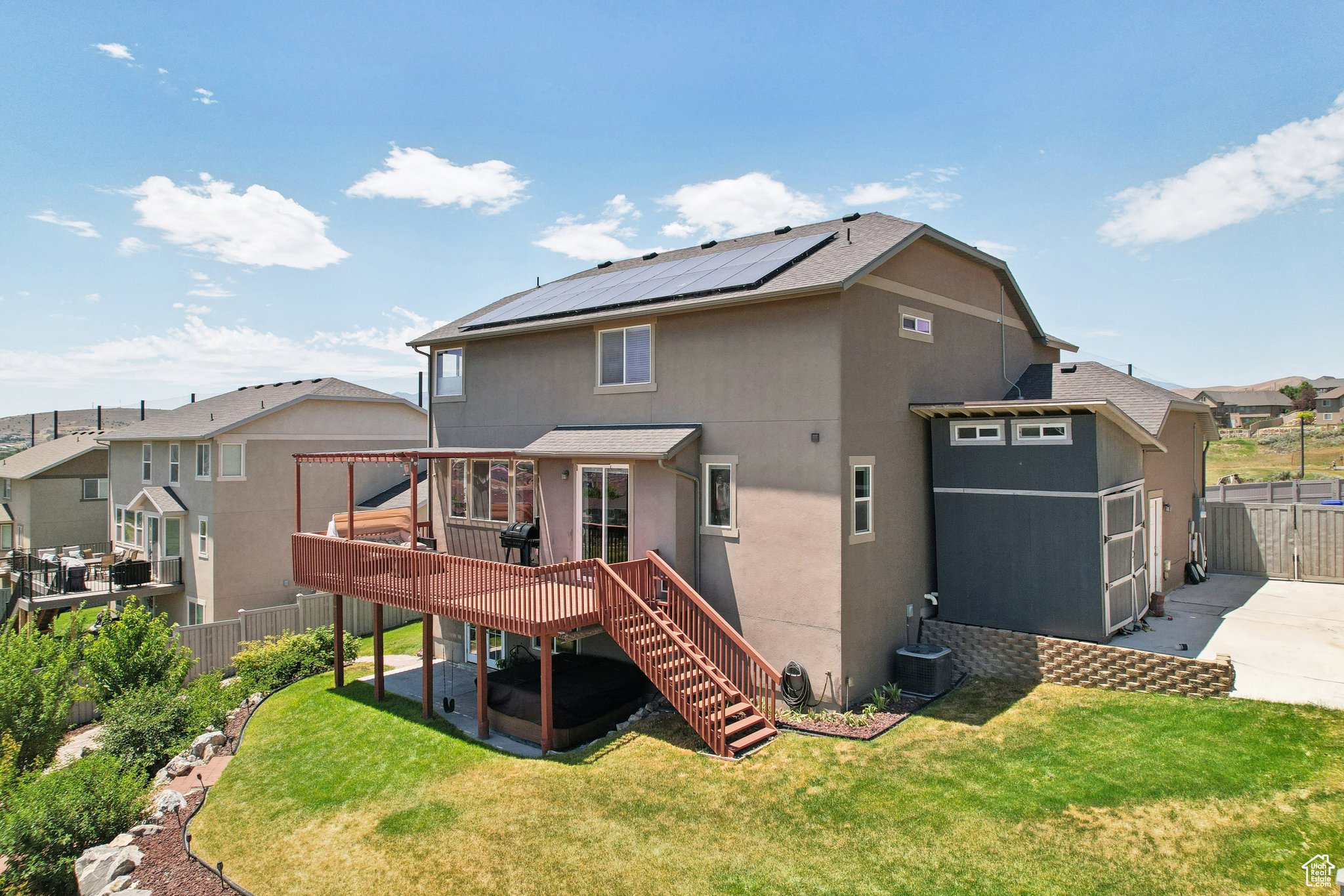 Rear view of property featuring a deck, a yard, solar panels, and central air condition unit