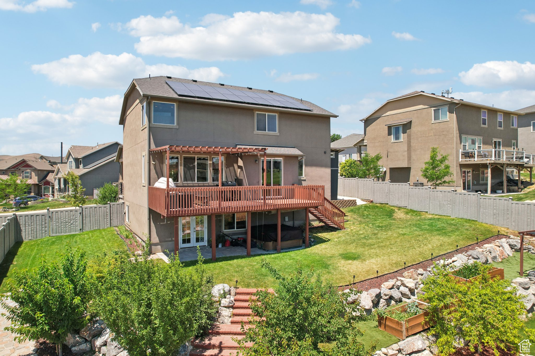 Back of house with a wooden deck, a lawn, a balcony, and solar panels