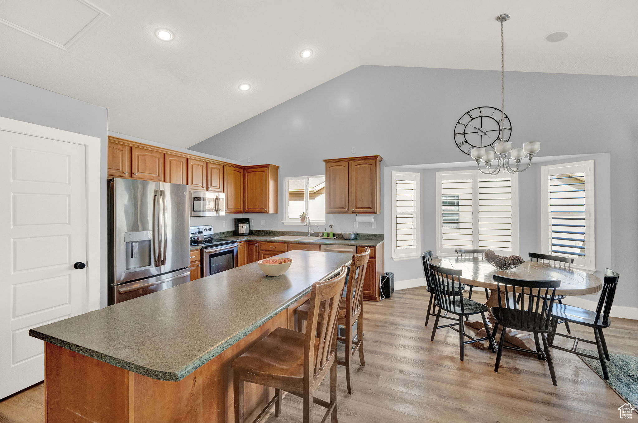 Kitchen featuring high vaulted ceiling, light hardwood / wood-style flooring, a chandelier, stainless steel appliances, and a kitchen island