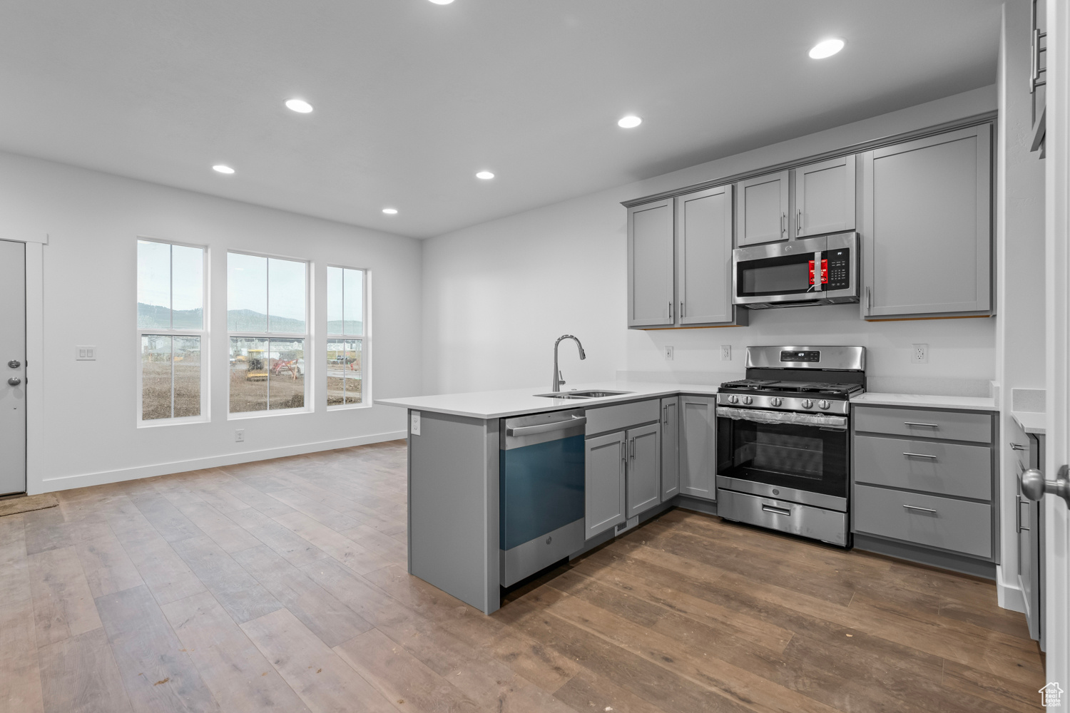 Kitchen featuring gray cabinets, kitchen peninsula, appliances with stainless steel finishes, sink, and hardwood / wood-style flooring