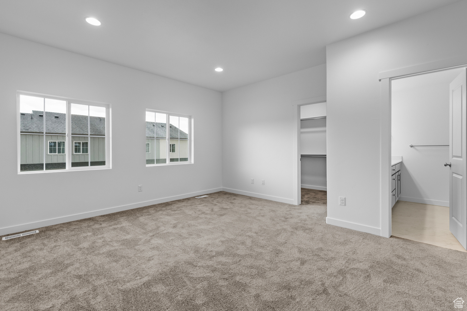 Unfurnished bedroom with light colored carpet, ensuite bath, a walk in closet, and a closet