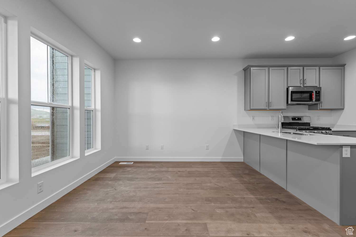 Kitchen with appliances with stainless steel finishes, light hardwood / wood-style floors, gray cabinets, kitchen peninsula, and a kitchen breakfast bar