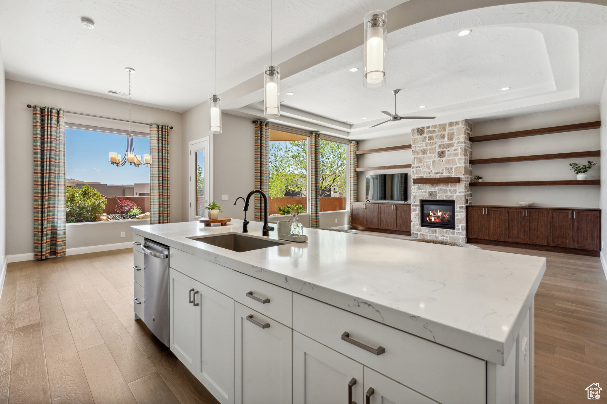 Kitchen featuring stainless steel dishwasher, sink, a center island with sink, and a stone fireplace