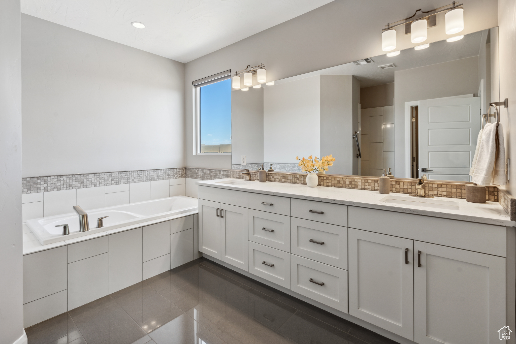 Bathroom featuring oversized vanity, tiled tub, tile floors, and dual sinks