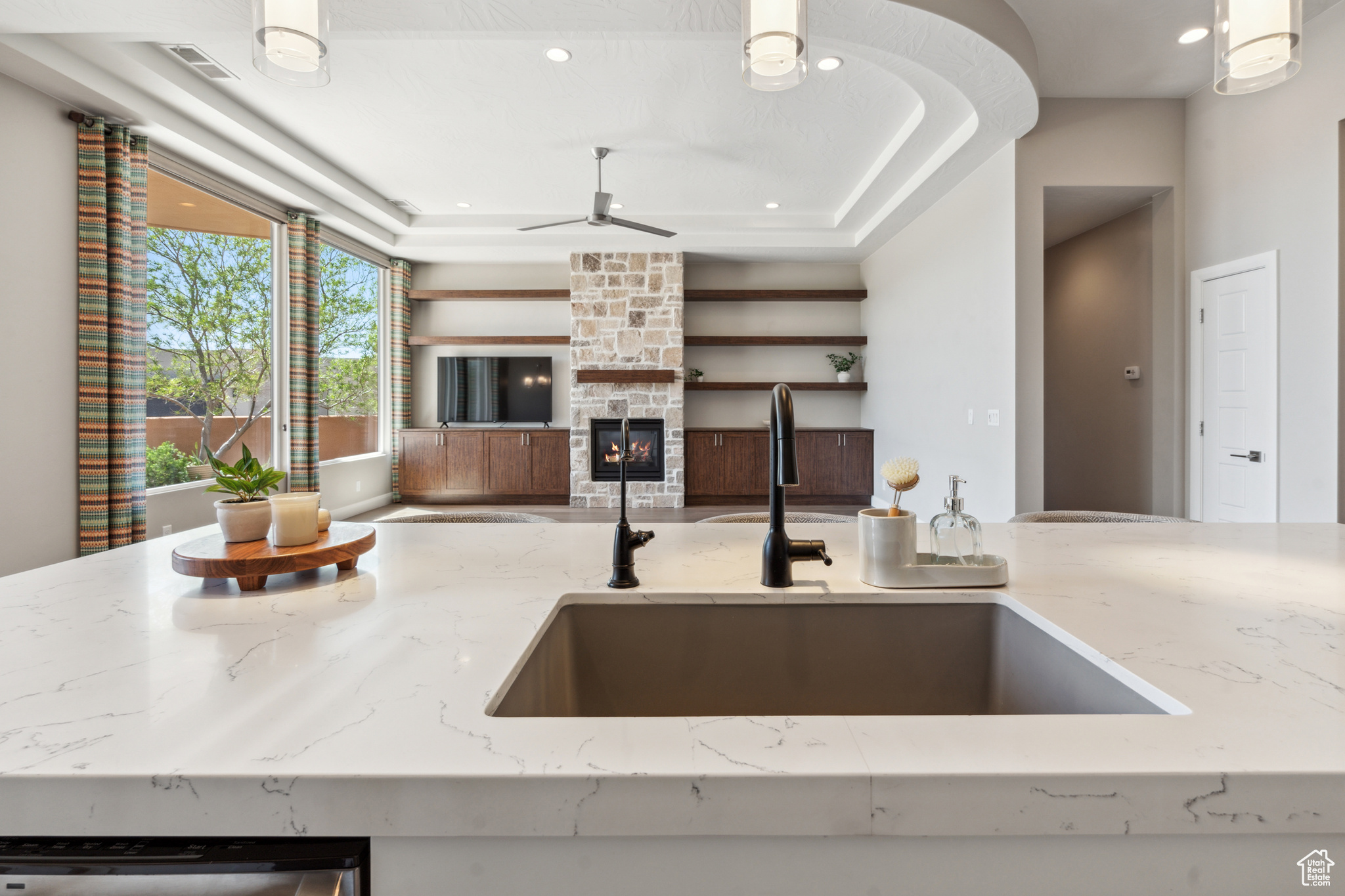Kitchen with ceiling fan, light stone counters, a fireplace, sink, and pendant lighting
