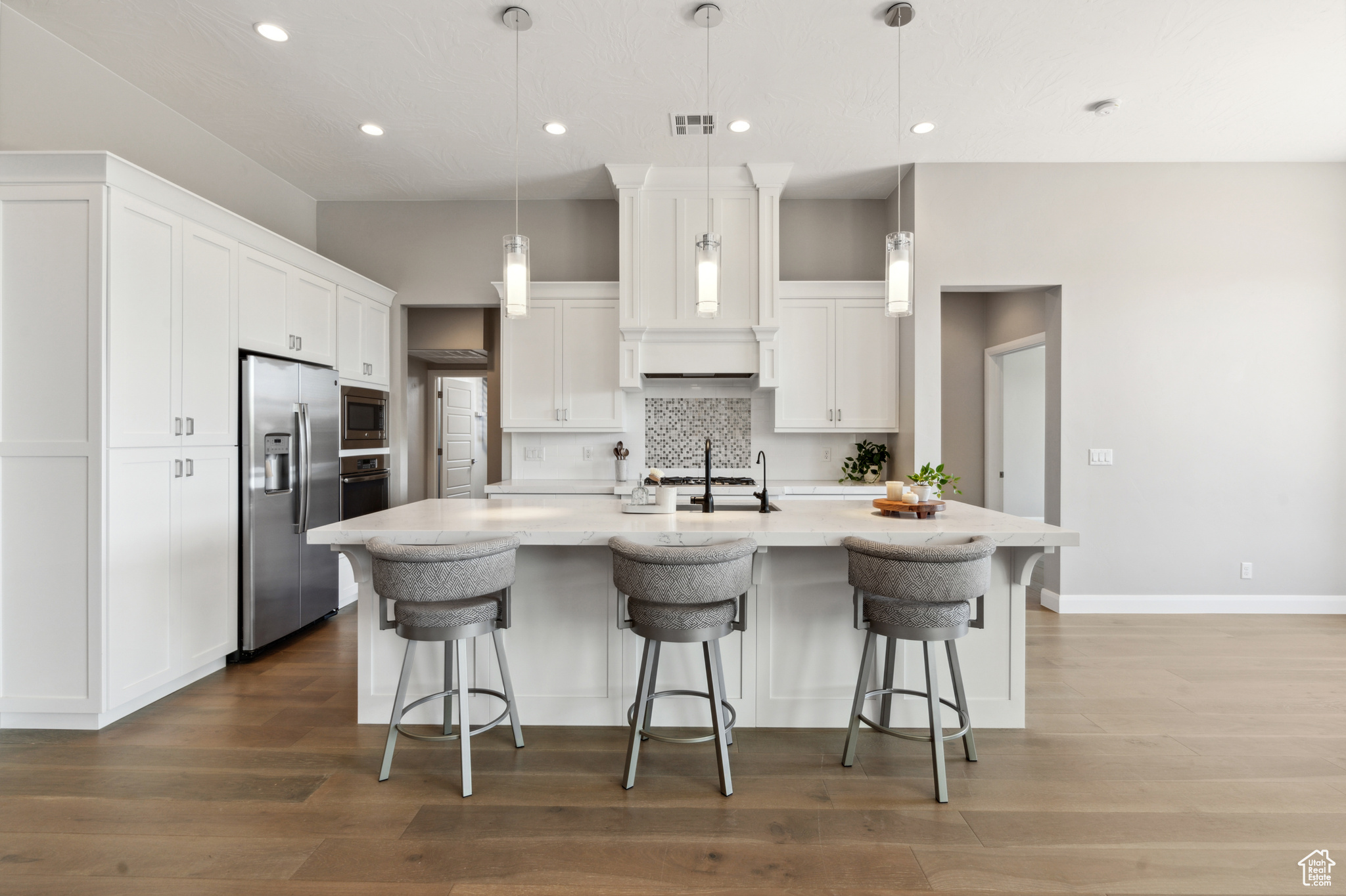 Kitchen with decorative light fixtures, wood-type flooring, white cabinets, and stainless steel appliances