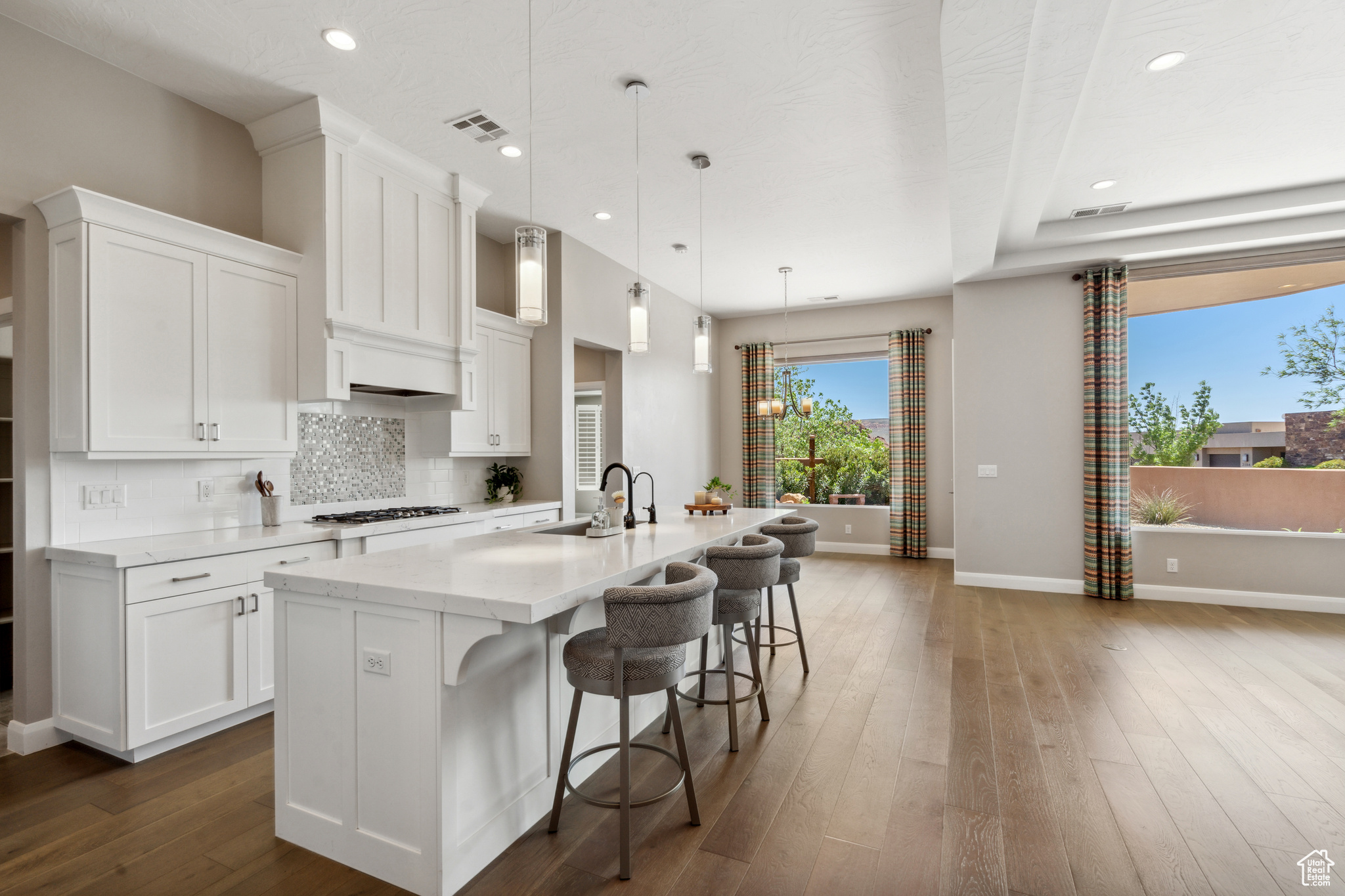 Kitchen with a wealth of natural light, dark hardwood / wood-style flooring, hanging light fixtures, and a center island with sink