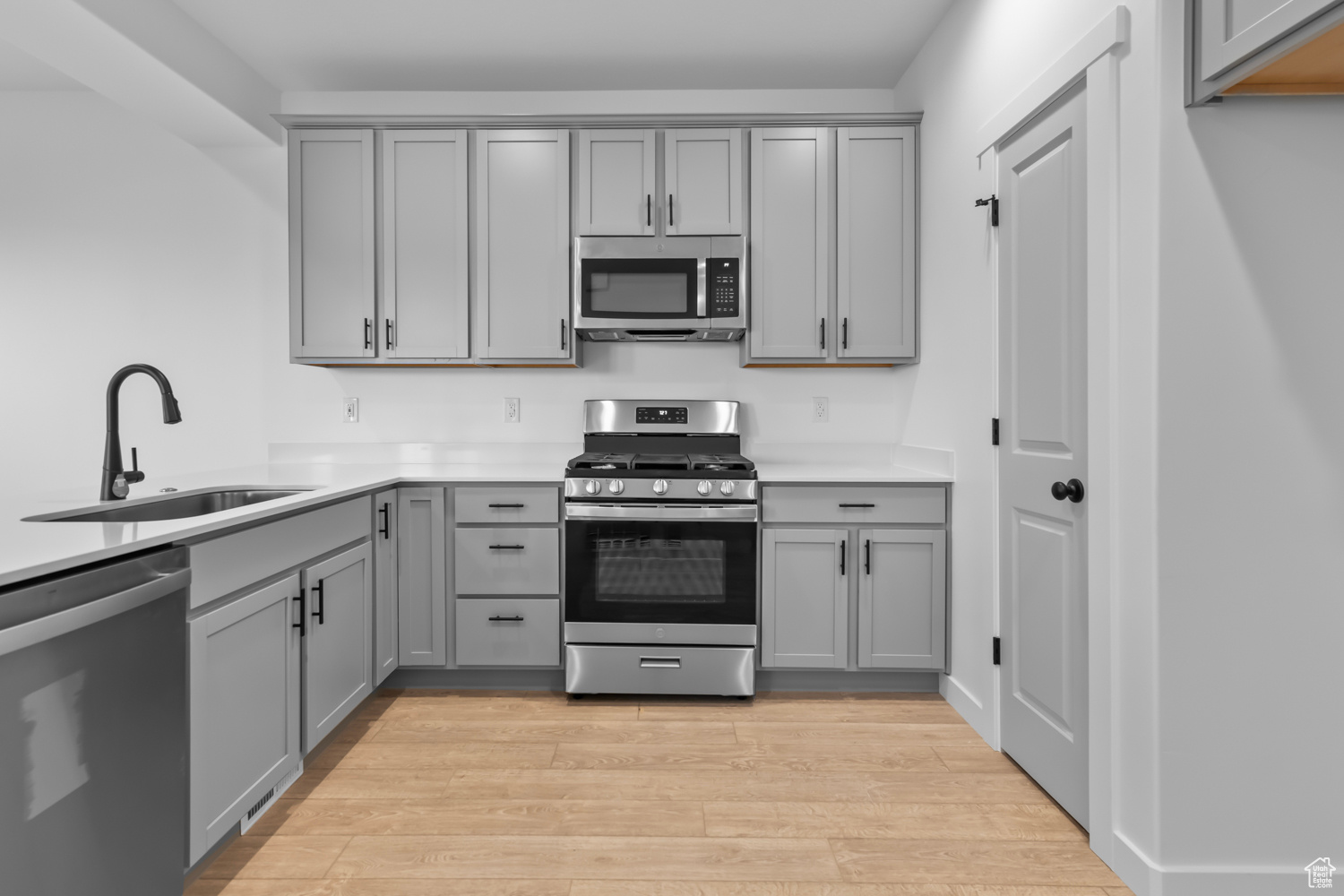 Kitchen featuring gray cabinets, sink, stainless steel appliances, and light wood-type flooring