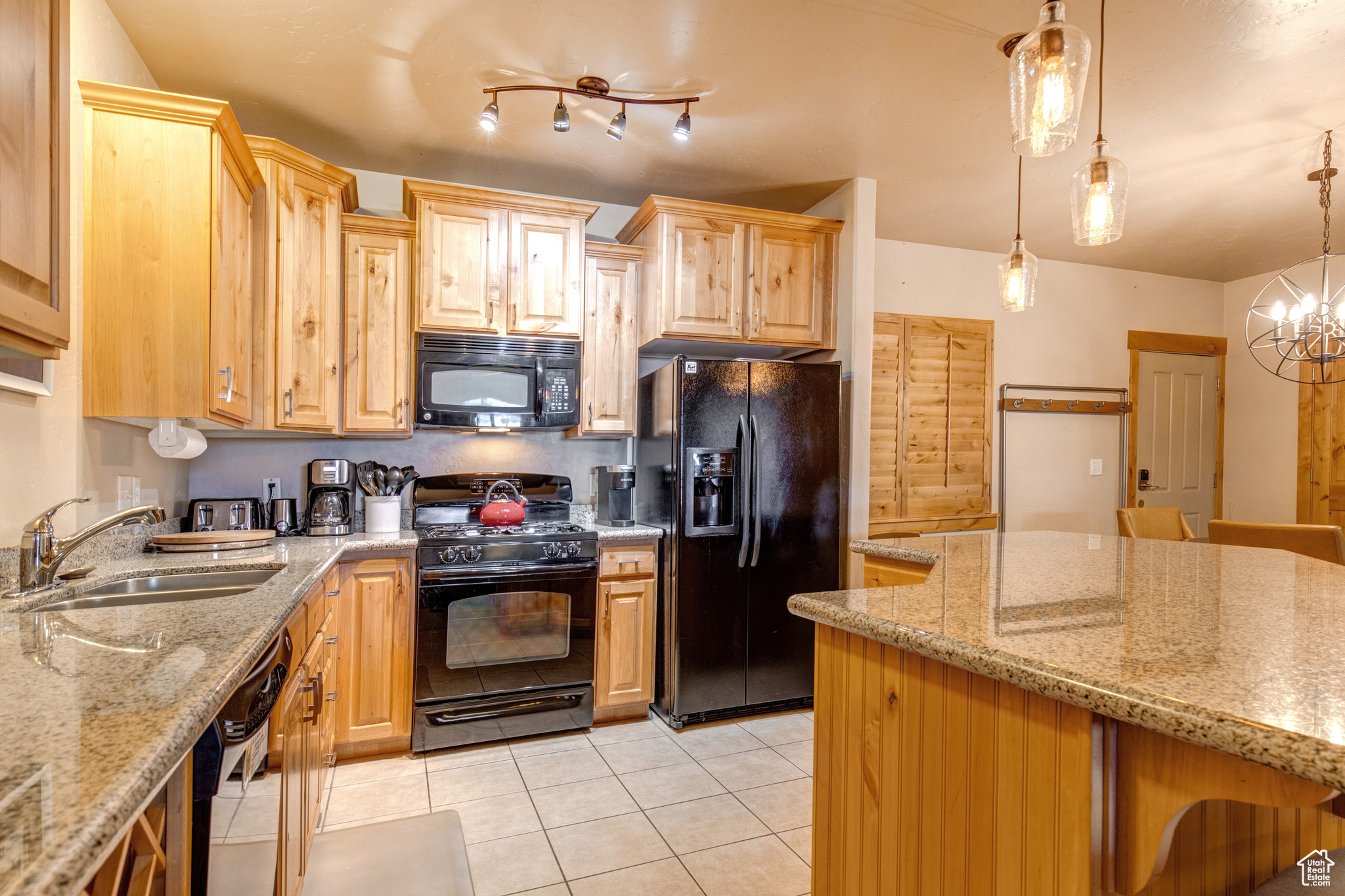 Kitchen with black appliances, light stone counters, pendant lighting, sink, and light tile floors