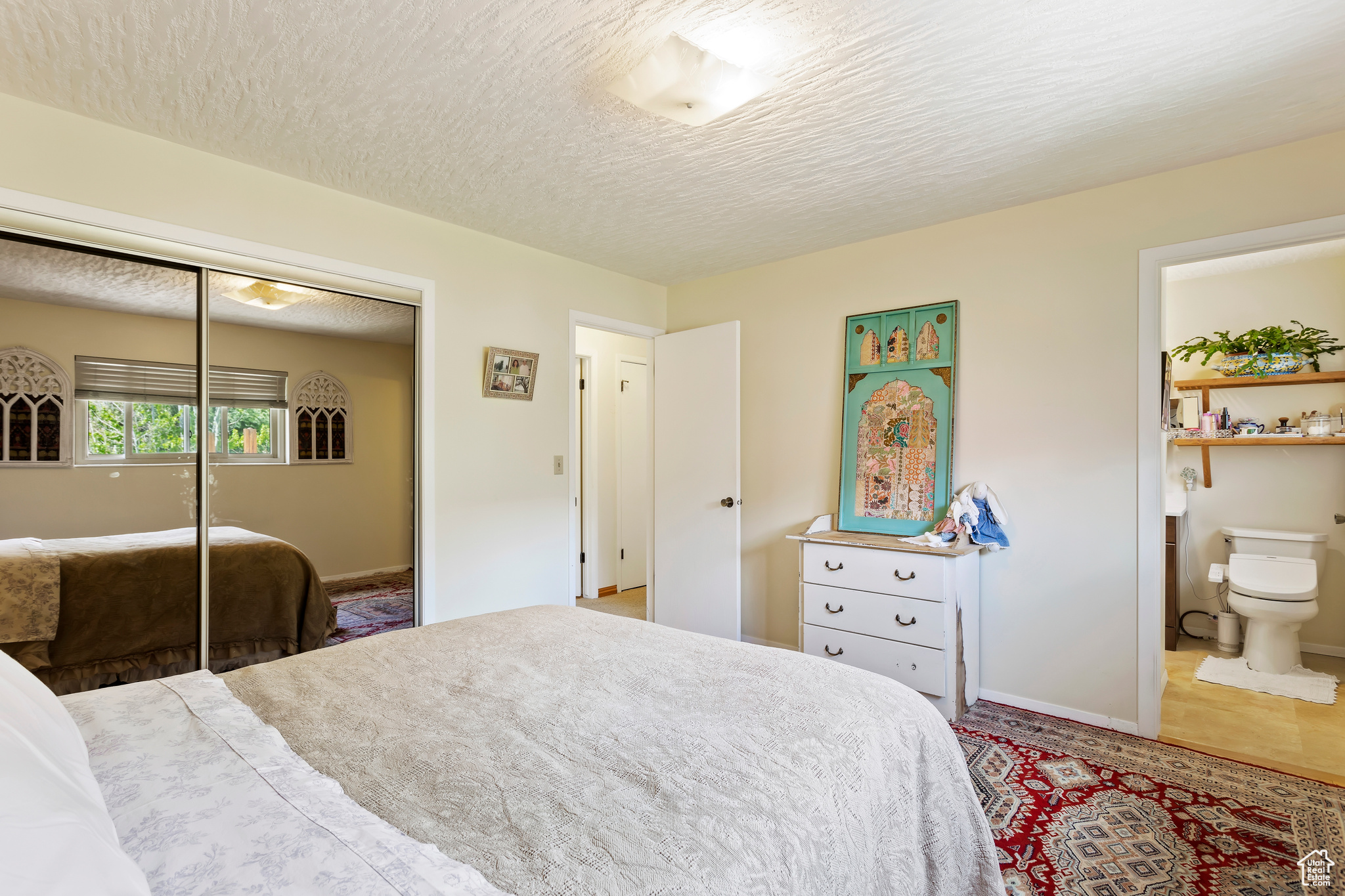 Bedroom featuring ensuite bath, tile floors, a closet, and a textured ceiling