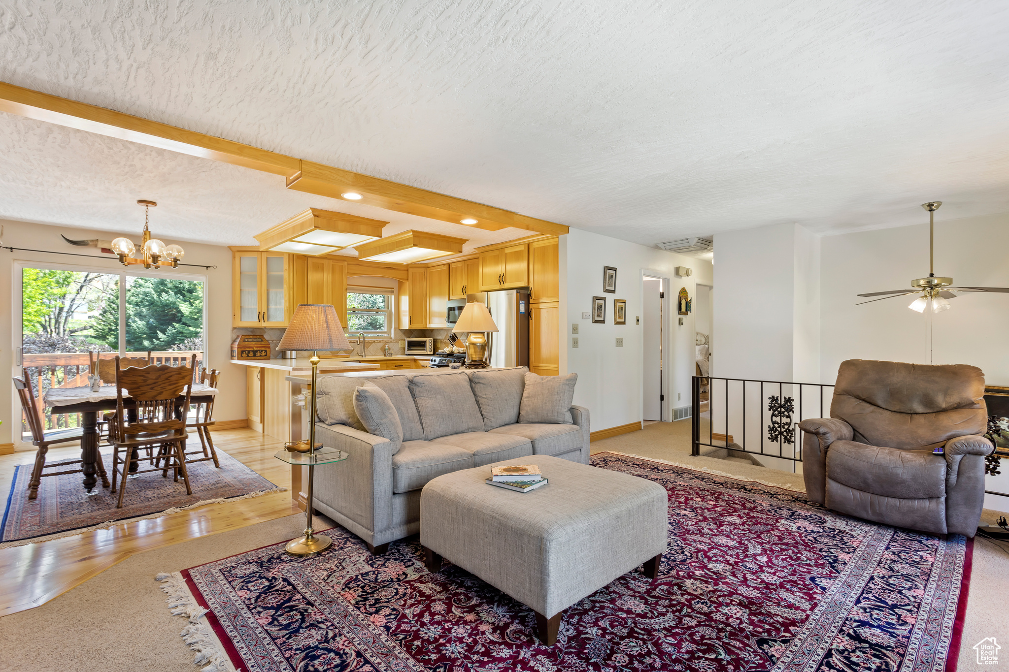 Living room with ceiling fan with notable chandelier, a textured ceiling, and beamed ceiling