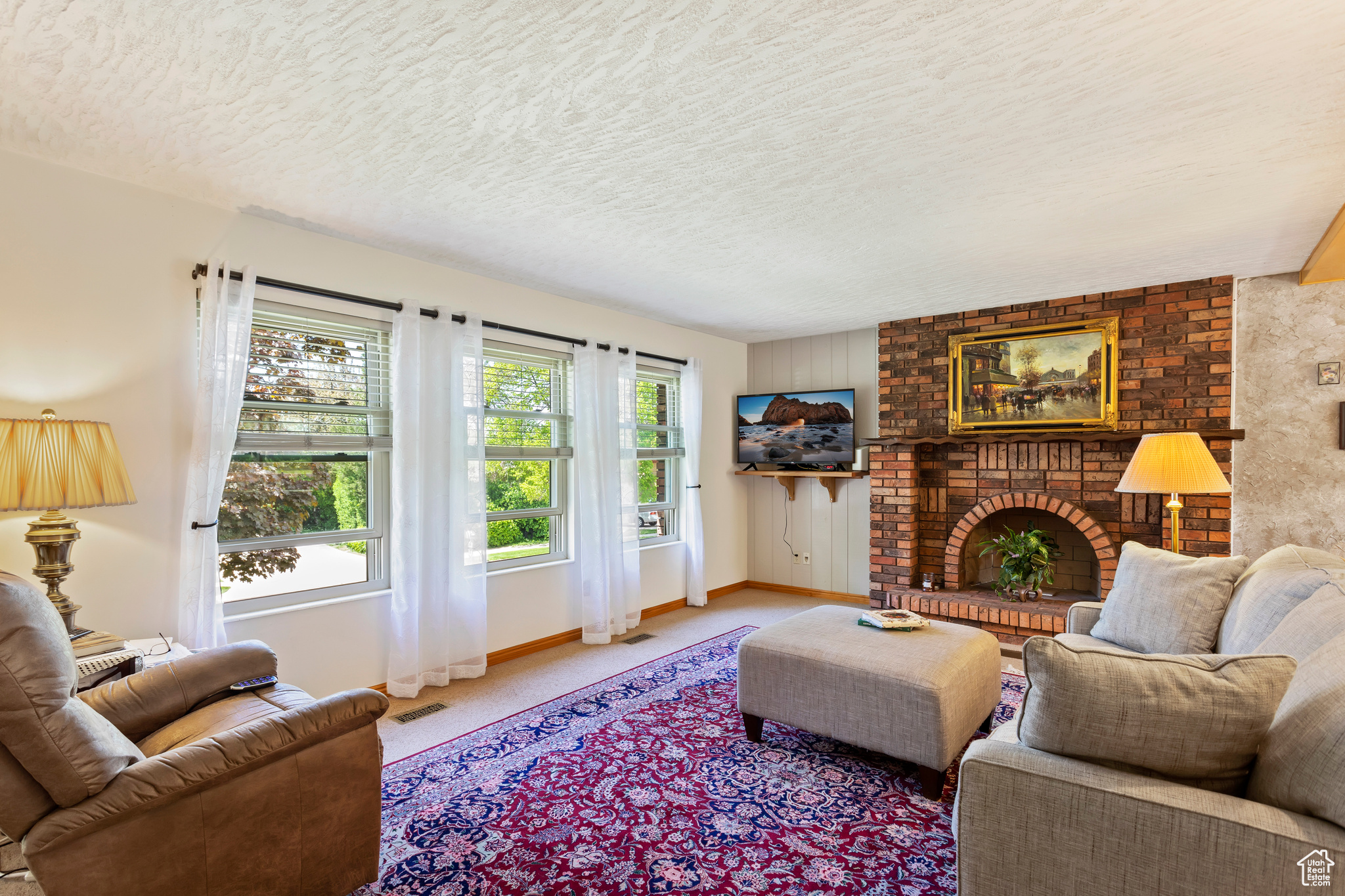 Carpeted living room with brick wall, a brick fireplace, and a textured ceiling