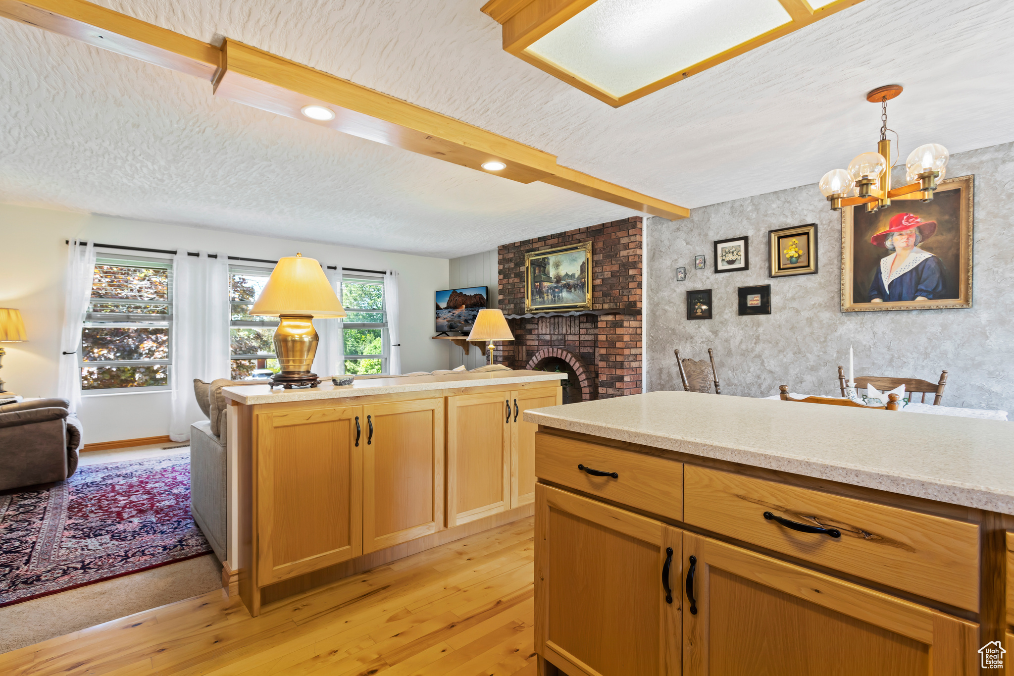 Kitchen with a brick fireplace, a textured ceiling, light wood-type flooring, decorative light fixtures, and a chandelier