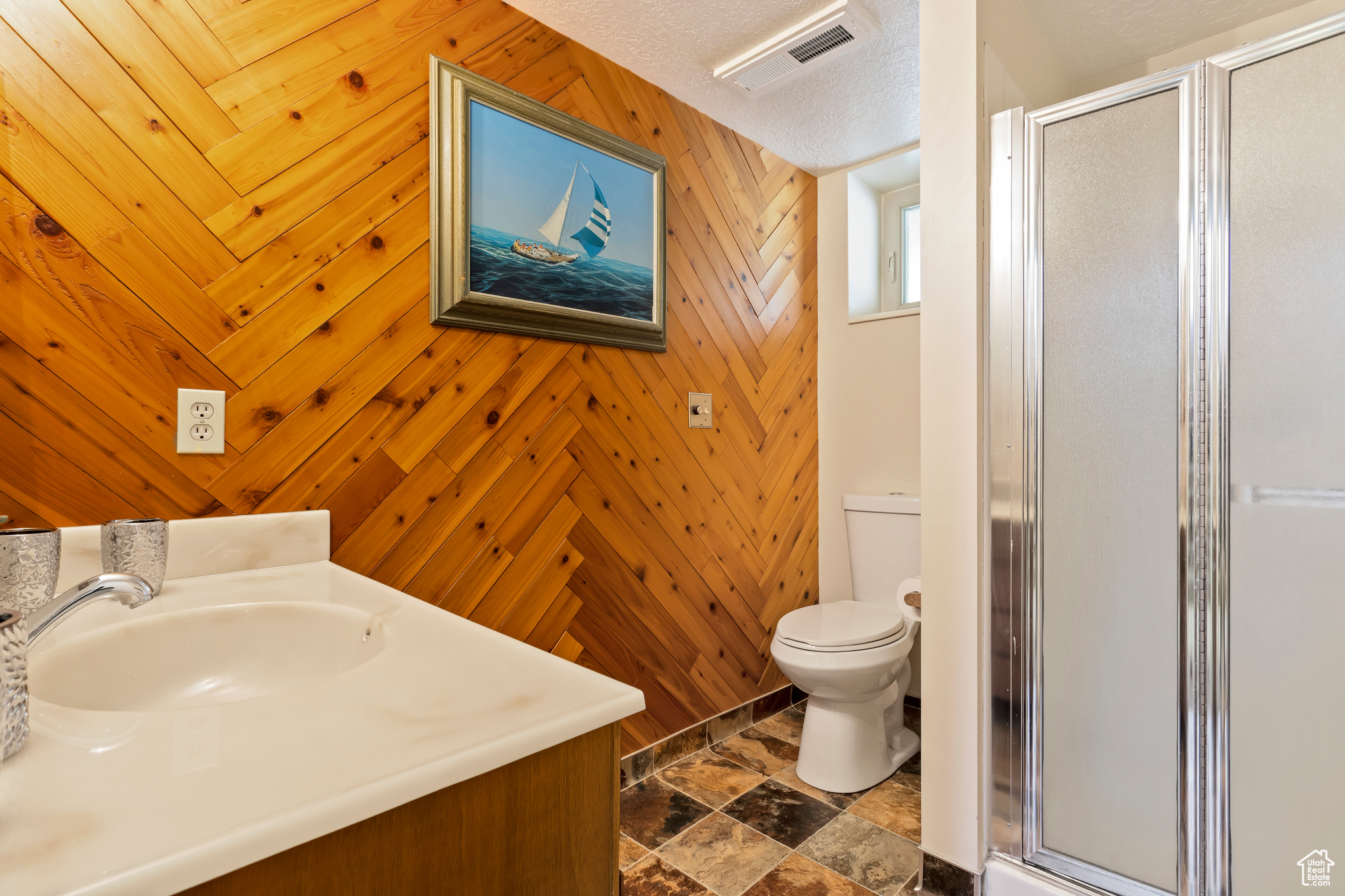 Bathroom with a textured ceiling, walk in shower, toilet, wood walls, and vanity