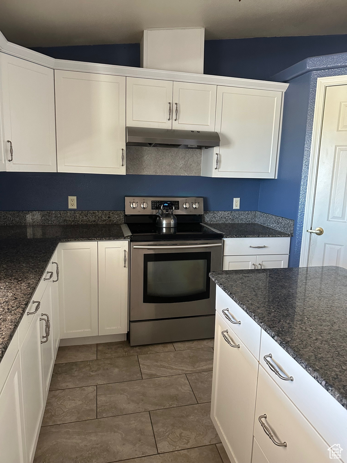 Kitchen with dark tile patterned flooring, white cabinets, dark stone countertops, and stainless steel electric range