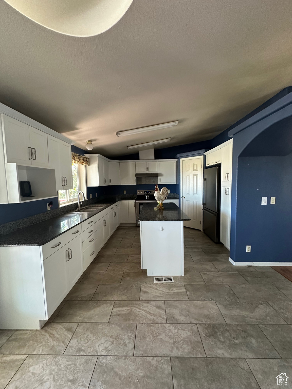 Kitchen featuring a kitchen island, white cabinets, light tile patterned floors, sink, and stainless steel fridge