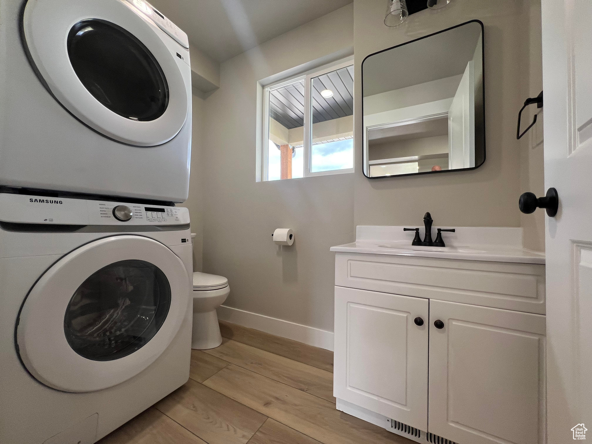 Laundry area with sink, light hardwood / wood-style flooring, and stacked washer and clothes dryer