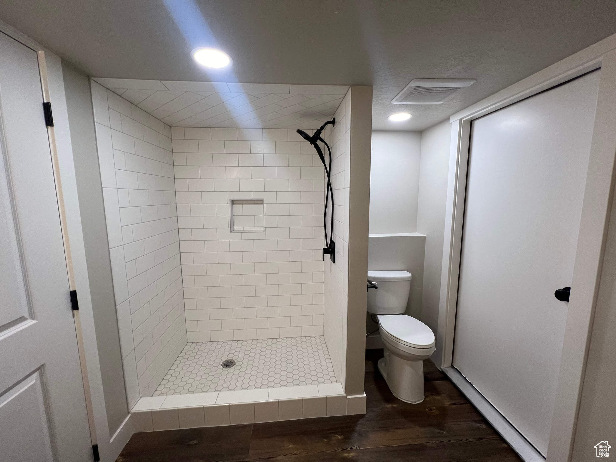 Bathroom with hardwood / wood-style floors, a tile shower, and toilet