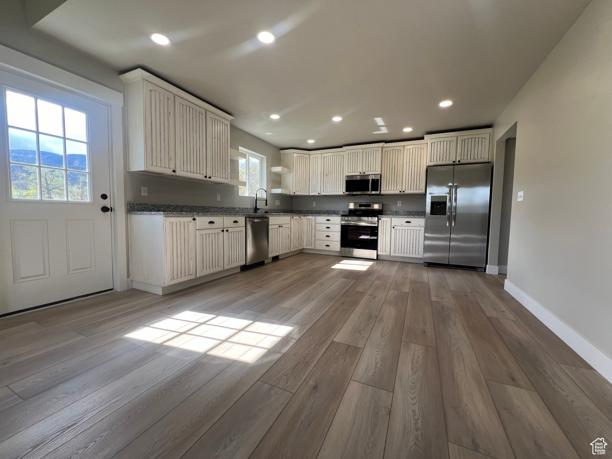 Kitchen with sink, appliances with stainless steel finishes, white cabinets, and hardwood / wood-style floors