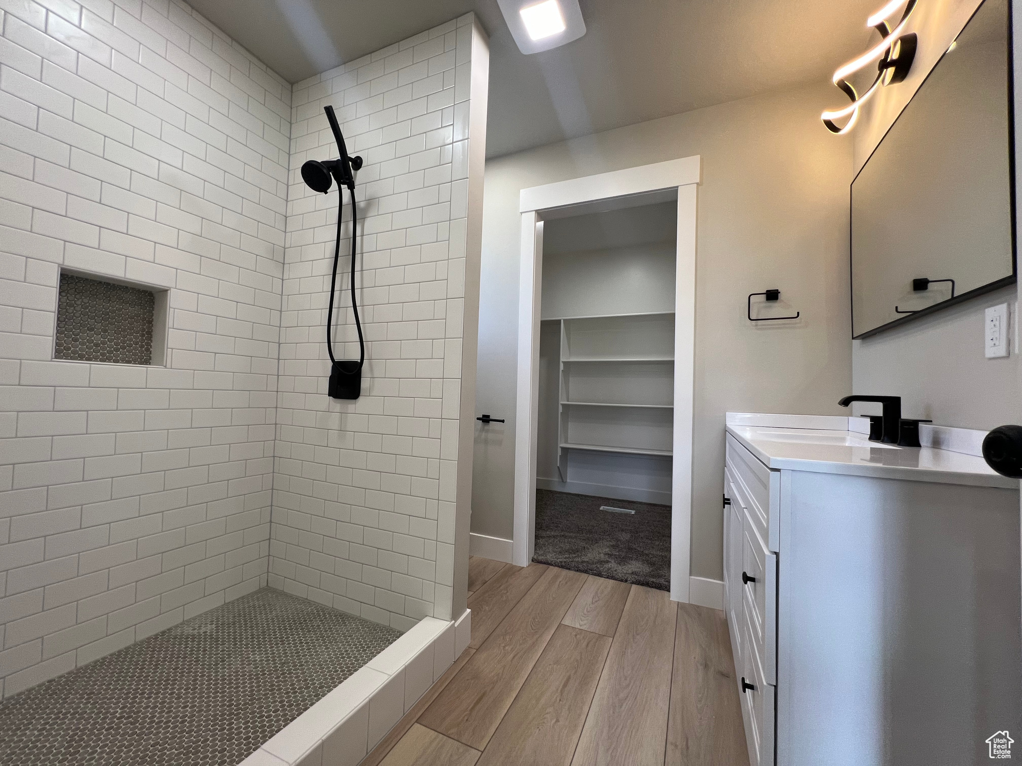 Bathroom featuring wood-type flooring, vanity with extensive cabinet space, and a tile shower