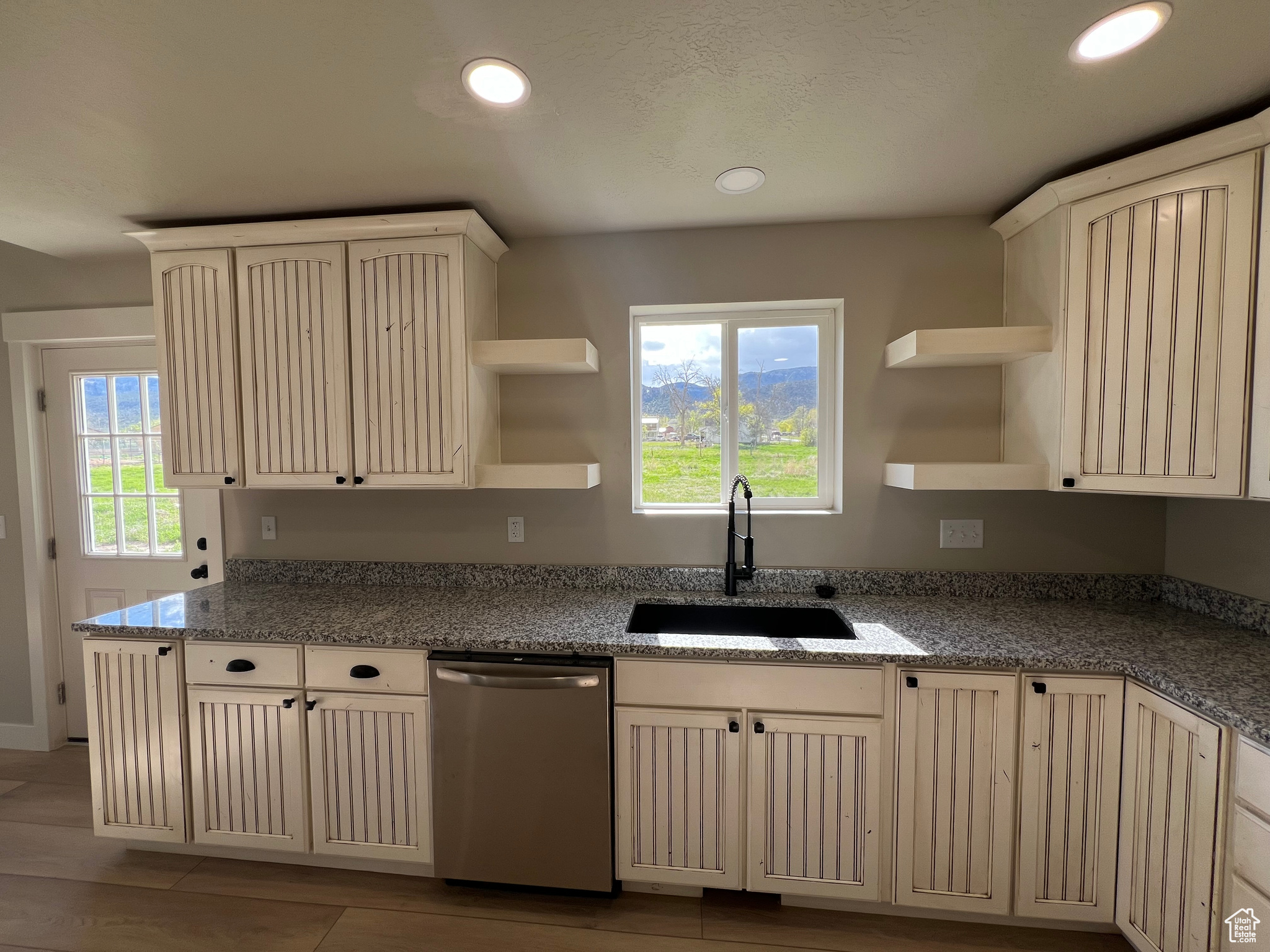 Kitchen with dark stone counters, dishwasher, sink, and light wood-type flooring