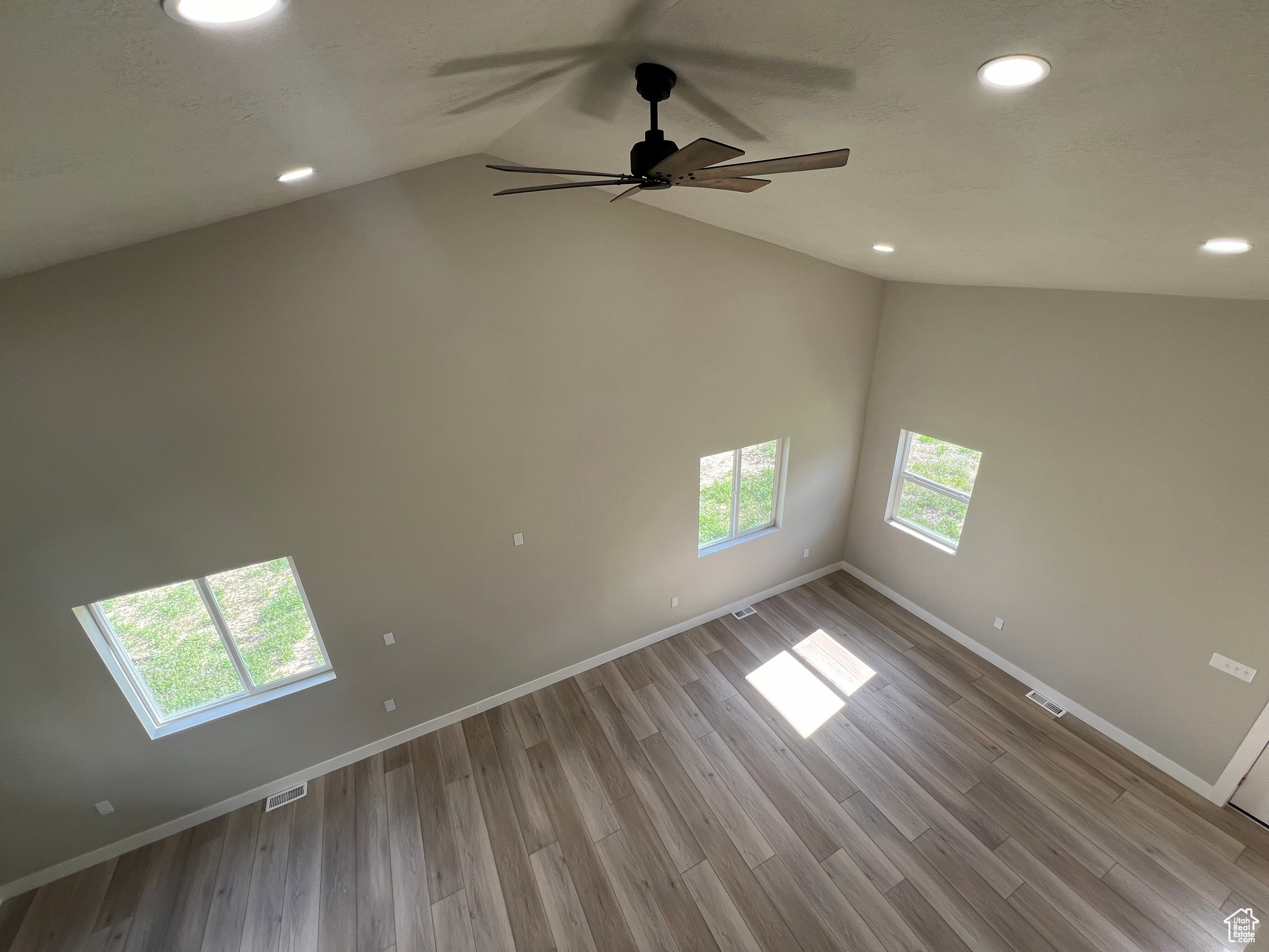 Unfurnished room featuring a skylight, high vaulted ceiling, ceiling fan, and light wood-type flooring