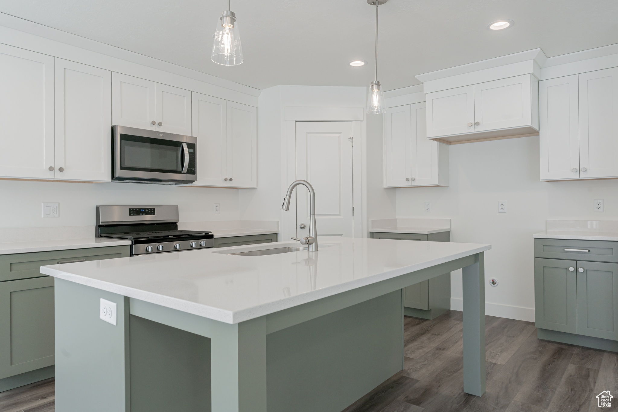 Kitchen featuring hardwood / wood-style floors, hanging light fixtures, stainless steel appliances, and an island with sink