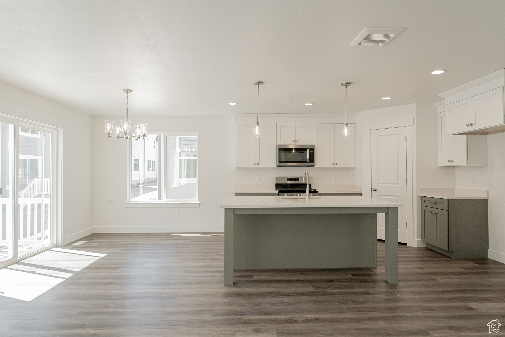 Kitchen with dark hardwood / wood-style flooring, pendant lighting, appliances with stainless steel finishes, an island with sink, and white cabinets