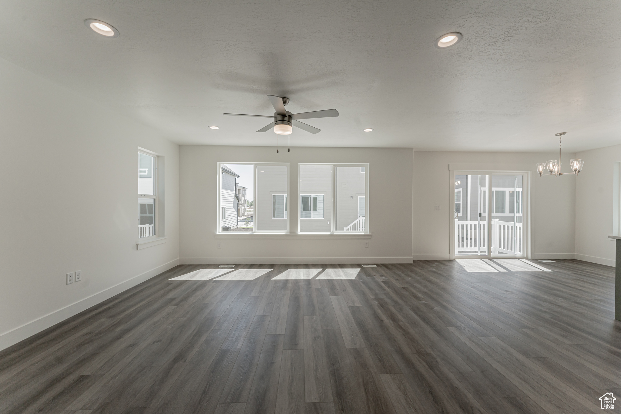 Unfurnished living room featuring ceiling fan with notable chandelier, dark wood-type flooring, and a textured ceiling