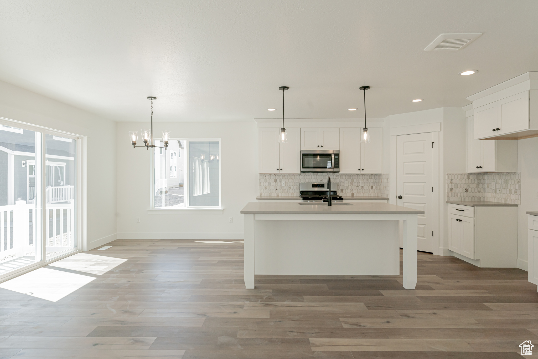 Kitchen featuring white cabinets, appliances with stainless steel finishes, light hardwood / wood-style floors, an island with sink, and pendant lighting