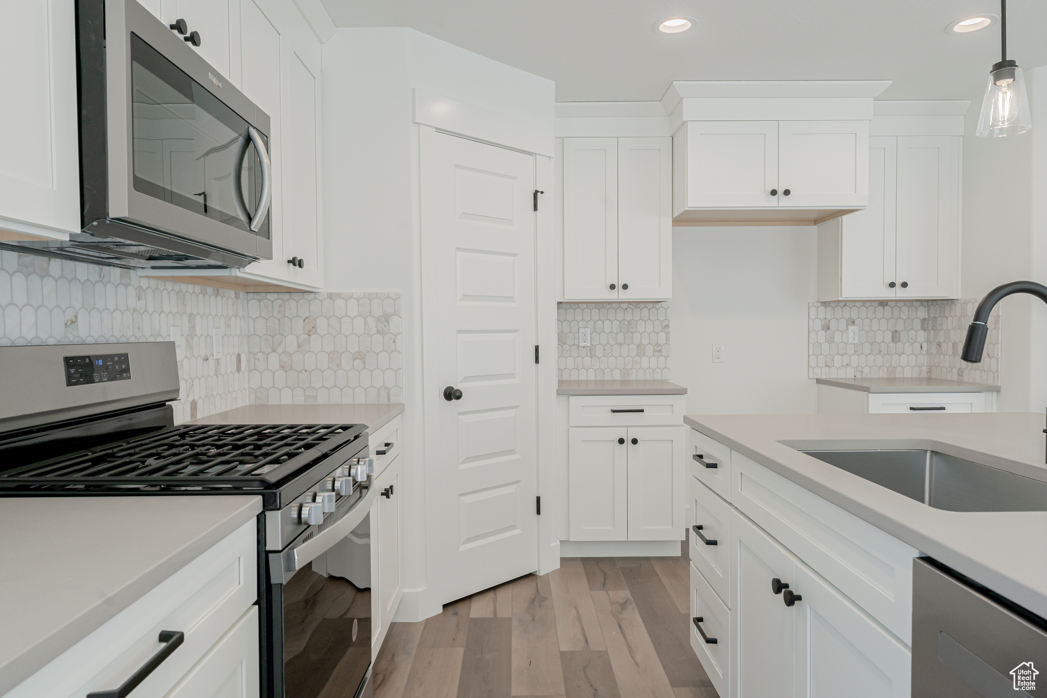 Kitchen with light wood-type flooring, pendant lighting, stainless steel appliances, sink, and white cabinets