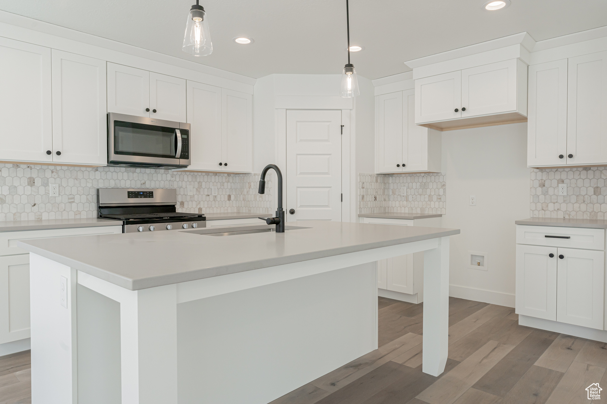 Kitchen with a center island with sink, light wood-type flooring, decorative light fixtures, and appliances with stainless steel finishes